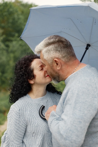 Close up romantic couple kissing in an autumn park. Man and woman wearing blue sweaters. Woman is brunette and man is gray.