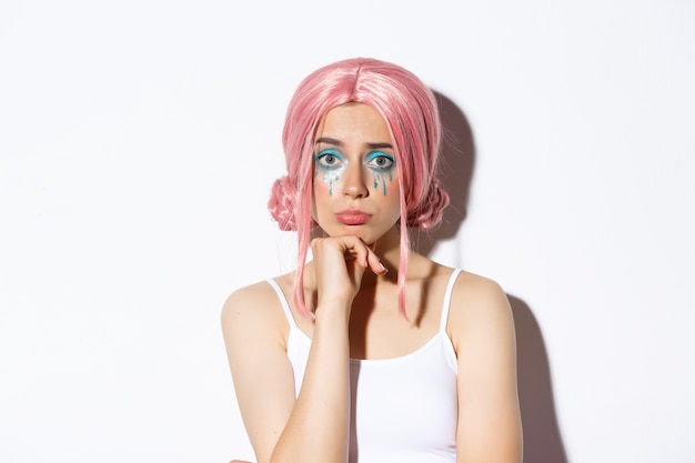 Close-up of sad cute girl with halloween makeup and pink wig looking upset, sulking while standing.