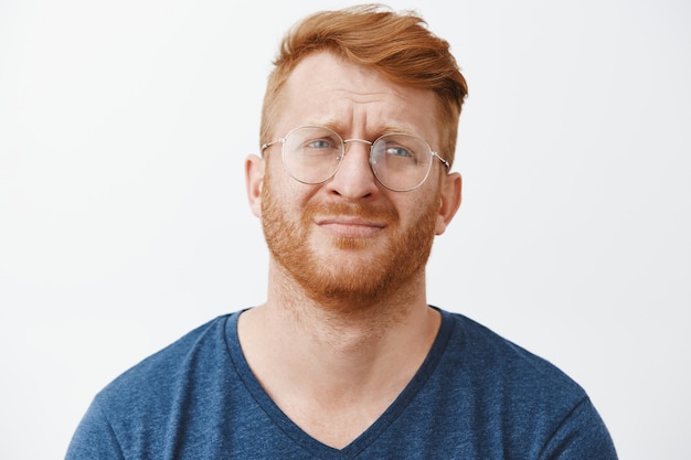 Close-up of sad and miserable redhead bearded man in glasses whining, looking upset