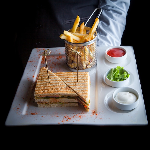 Close-up sandwich with fried potatoes and sauce on a white plate at the waiter