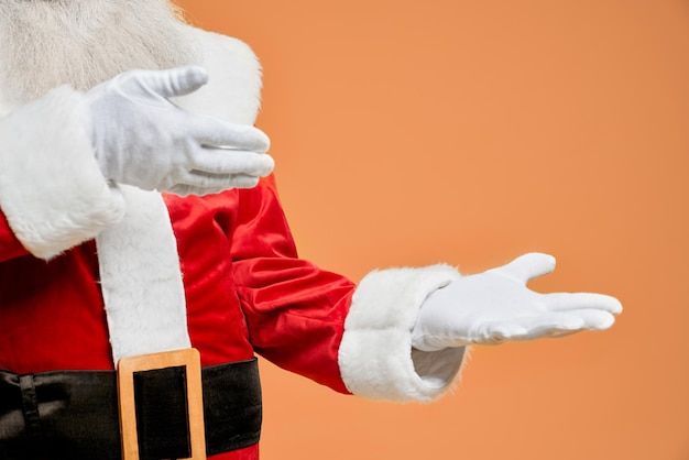 Close up of santa claus hands in white gloves with open palms and empty space posing in studio with orange background. place for text or advertisement of some product