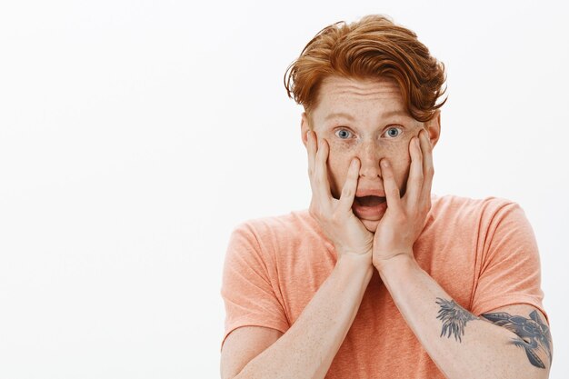 Close-up of scared insecure redhead man holding hands on face shocked, gasping startled