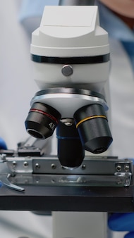 Close up of scientific microscope in laboratory and specialist hands using lens with magnifying glass for dna test and analysis. doctor with gloves analyzing sample for investigation