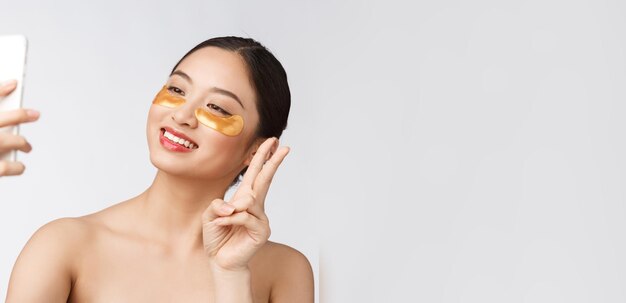 Close up selfie of beautiful happy woman with eye mask on faceWoman with eyes mask taking selfie with mobile phone at home enjoying relaxation and