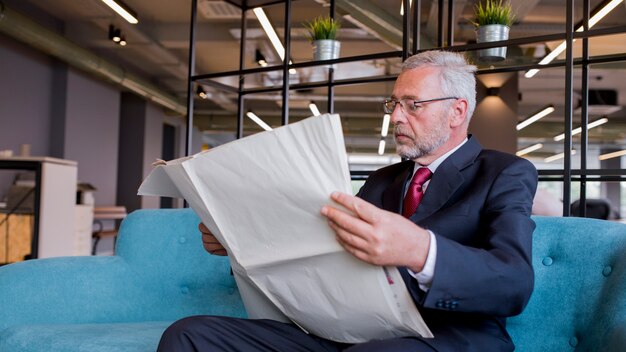 Close-up of senior businessman sitting on sofa reading newspaper in the office