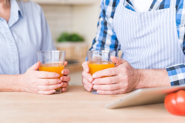 Close-up of senior couple holding glass of juice on wooden table