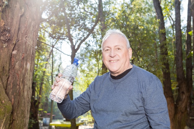 Крупным планом старший мужчина держит бутылку с водой