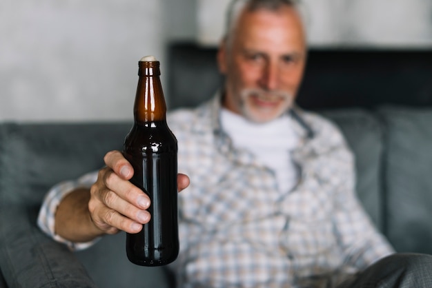 Foto gratuita primo piano di un uomo anziano che mostra bottiglia di birra con schiuma