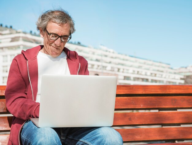 Primo piano di uomo anziano seduto sulla panchina utilizzando il computer portatile