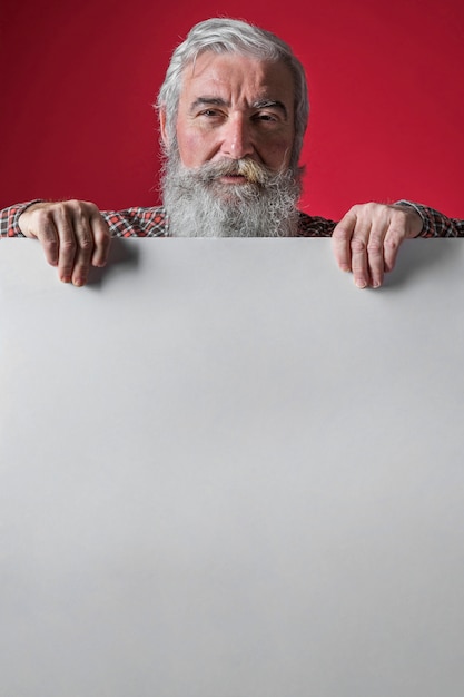 Free photo close-up of senior man standing behind the white placard against red backdrop