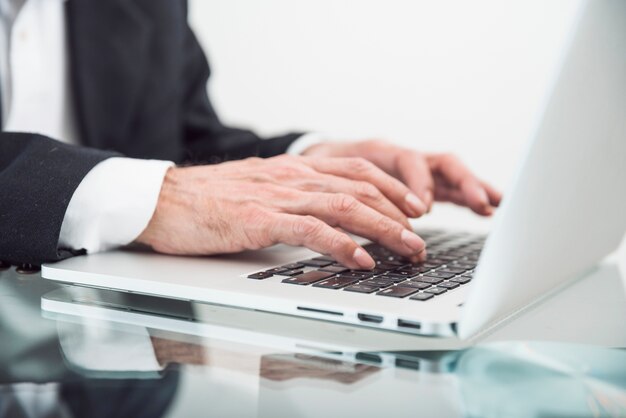 Close-up of senior man typing on laptop over the glass desk