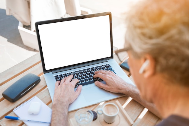 Close-up of senior man typing on laptop with white blank screen