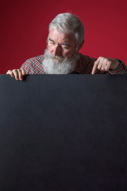 Крупный план старшего человека с седой бородой, указывая пальцем на пустой черный плакат