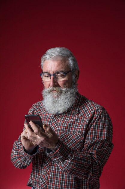 빨간색 배경에 휴대 전화 서를 사용하여 회색 수염을 가진 수석 남자의 근접