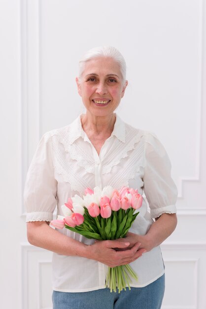 Крупный план старшей женщины, держащей букет цветов тюльпана, смотрящих на камеру