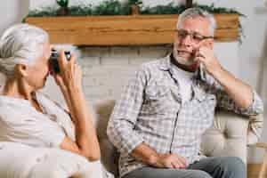 Free photo close-up of senior woman photographing her husband with camera sitting on sofa