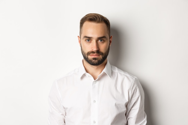 Close-up of serious businessman in white shirt looking at camera, standing confident.