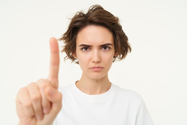 Foto gratuita il primo piano di una giovane donna seria mostra un gesto tabù di arresto con un dito che disapprova qualcosa che blocca