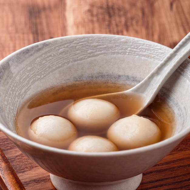 Close up of sesame big tangyuan (tang yuan, glutinous rice dumpling balls) with sweet syrup soup in a bowl on wooden table background for winter solstice festival food. Premium Photo