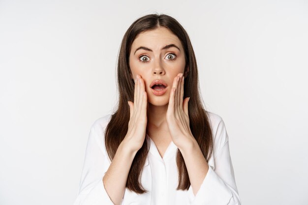 Close up of shocked woman gasping, looking stunned and speechless, gasping startled, standing over white background.