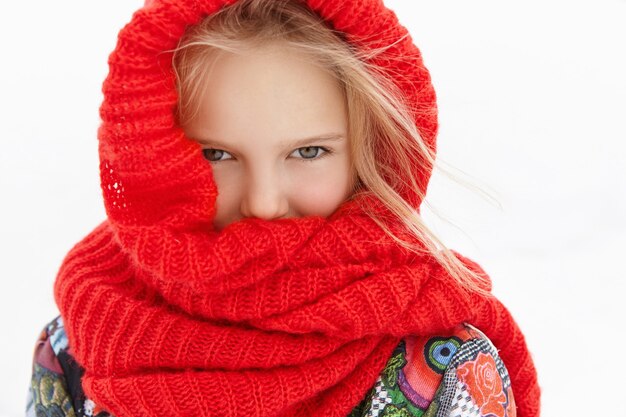 Close up shot of adorable female child feeling cold while having walk outdoors