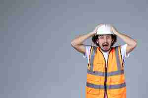 Free photo close up shot of afraid male architect in warning vest with safety helmet and holding it over gray wave wall