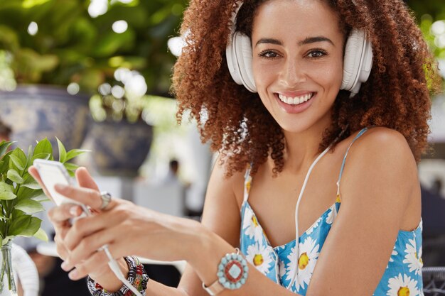 Крупным планом афроамериканская девушка общается в чате с друзьями в социальных сетях, просматривает веб-сайт, слушает любимую звуковую песню из плейлиста в наушниках