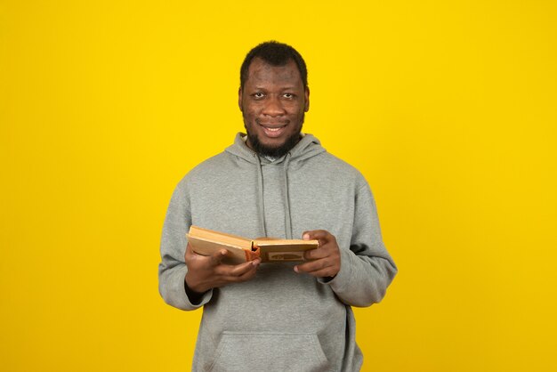 クローズアップショットアフリカ系アメリカ人の笑顔の男は、彼の手で本を読んで、黄色の壁の上に立っています。