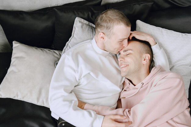 Close up shot of appealing happy gay couple smiling. Resting in bed.