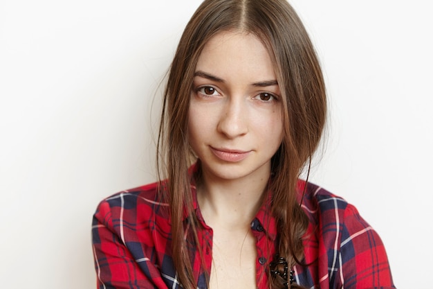 Close-up shot of attractive brunette student girl with messy hairstyle dressed in stylish checkered shirt