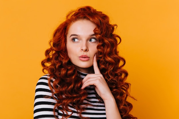 Free photo close-up shot of attractive girl in striped t-shirt looking pensively to side against orange space.