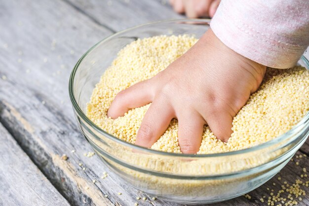 Крупным планом снимок руки ребенка, положенной в миску из свежего цельного зерна амарата