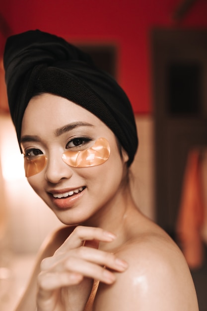 Close-up shot of brown-eyed woman in towel on her head and with patches