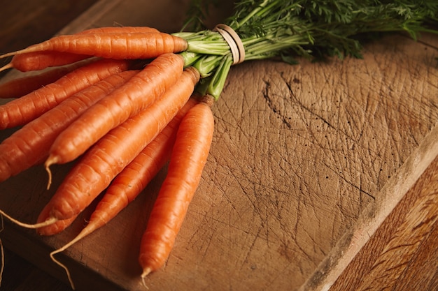 Close up shot of a bunch of fresh ripe carrots on an old chopping board with deep cuts