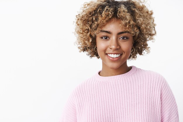 Close-up shot of charismatic friendly-looking happy nice dark-skinned girl with pierced nose, perfect smile standing delighted and cute over white wall in sweater enjoying family holiday dinner