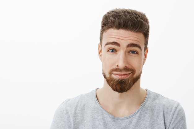 Close-up shot of charming kind and charismatic happy bearded man with moustache raising eyebrows and smirking with delight and tender feelings loooking with love and joy