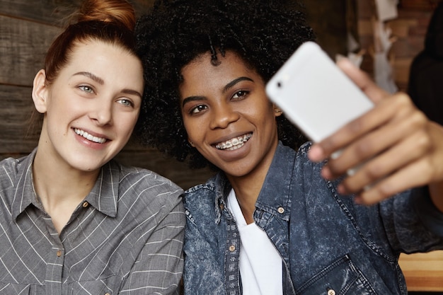 Close up shot of charming redhead lesbian with hair knot posing for selfie together