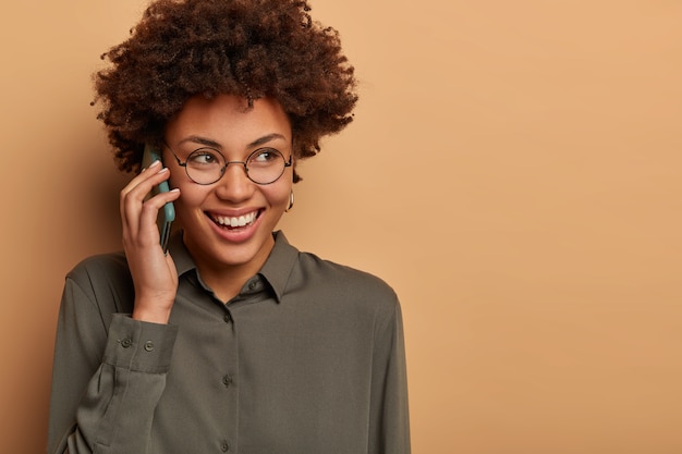 Крупным планом - жизнерадостная афроамериканка, которая весело разговаривает по телефону, широко улыбается и задумчиво куда-то смотрит
