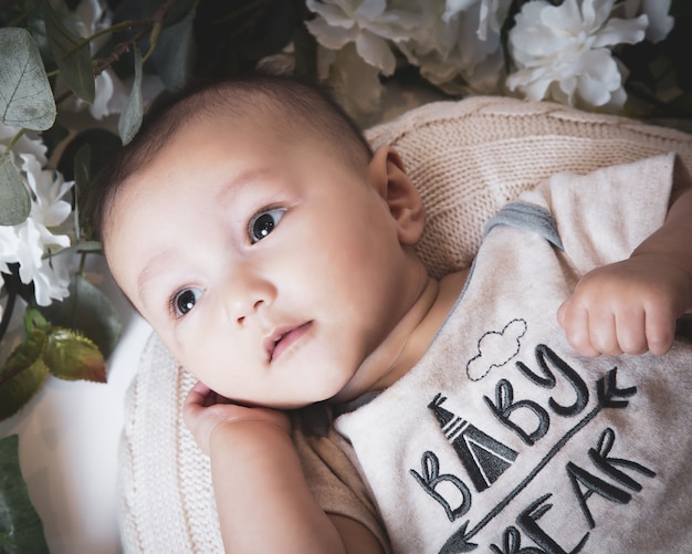 Close up shot of a cute Caucasian baby boy surrounded by flowers