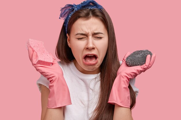 Close up shot of dejected young sullen woman cries desperately, has sorrowful expression, carries sponges