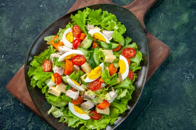 Close up shot of delicious salad with many fresh ingredients on wooden cutting board on black green mix colors background