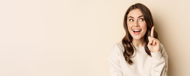 Close up shot of excited woman looking amazed with opened mouth standing over beige background