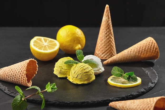 신선한 민트로 장식된 환상적인 천연 크림과 레몬 아이스크림의 클로즈업 샷은 검정색 배경 위에 어두운 석판 위에 제공됩니다.