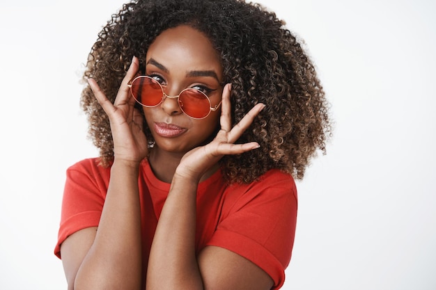 Free photo close-up shot of fashionable and glamour good-looking african-american woman in casual red t-shirt putting on red circle stylish glasses
