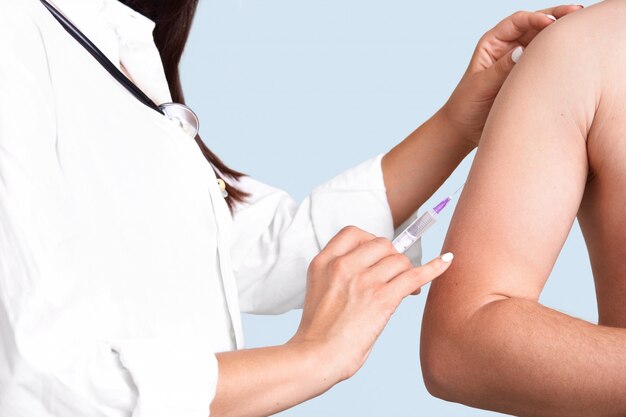 Free photo close up shot of female doctor`s hands makes vacciantion to patient, uses syringe, inject at upper arm, prevents serious disease, isolated over blue wall. selective focus. heathcare concept