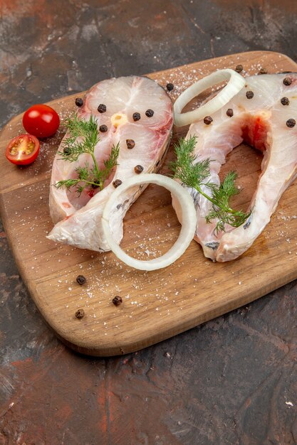 Close up shot of fresh raw fishes and pepper onion greens tomatoes on wooden cutting board on mix color surface