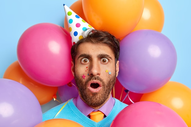 Close up shot of frightened guy surrounded by party balloons posing
