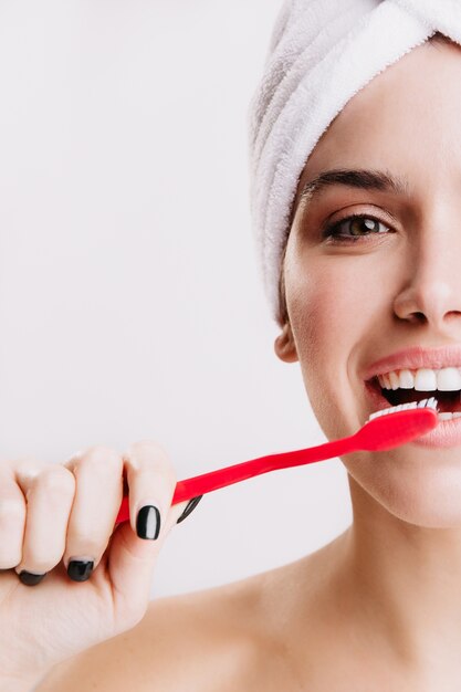 Close-up shot of half face of cheerful woman brushing her teeth on isolated wall.