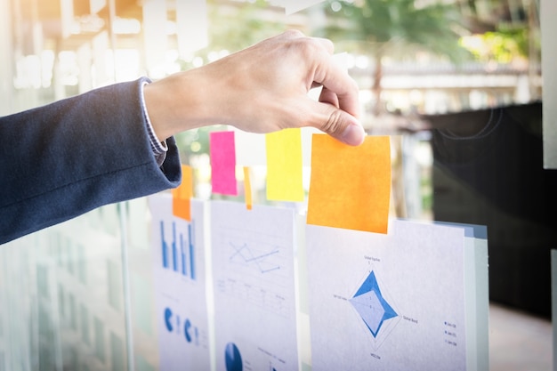 Close up shot of hands of business man sticking adhesive notes on glass wall in office.