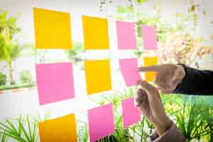 Free photo close up shot of hands of woman sticking adhesive notes on glass wall in office